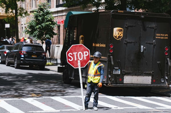 Construction worker holding a stop sign in front of a parked UPS truck on a street.